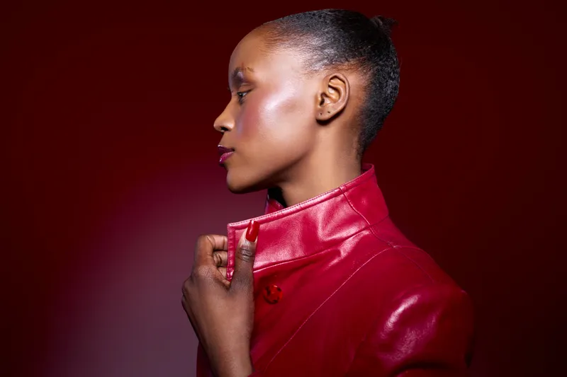 Profile of a young black African woman with dark skin wearing a red leather jacket on red background. Concept of fashion, beauty, elegance, and confident female model portrait.