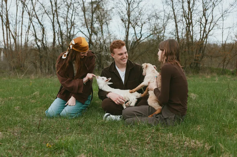 Goat, kid, outdoor, field, nature, laughter, interaction, friends, candid, sunlit, moment, meadow, relaxed, breeze, smiling, pose, companionship, pastoral, rural, joy, sunshine, family, season,