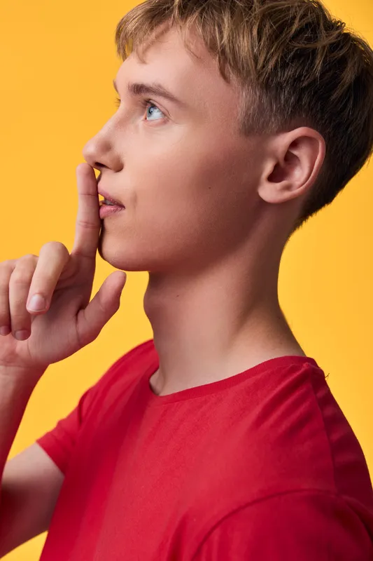 Thinking, silence, secrecy, gesture of shushing for quiet mood with youth in a red shirt against a warm yellow background, conveying hush and contemplation