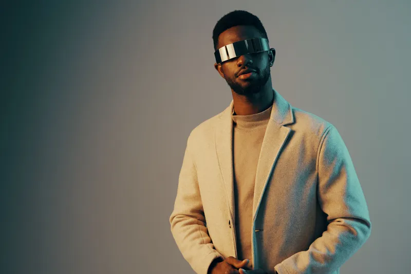 Stylish young man wearing futuristic sunglasses with a pastel colored background, conveying a modern aesthetic and confidence in fashion and technology