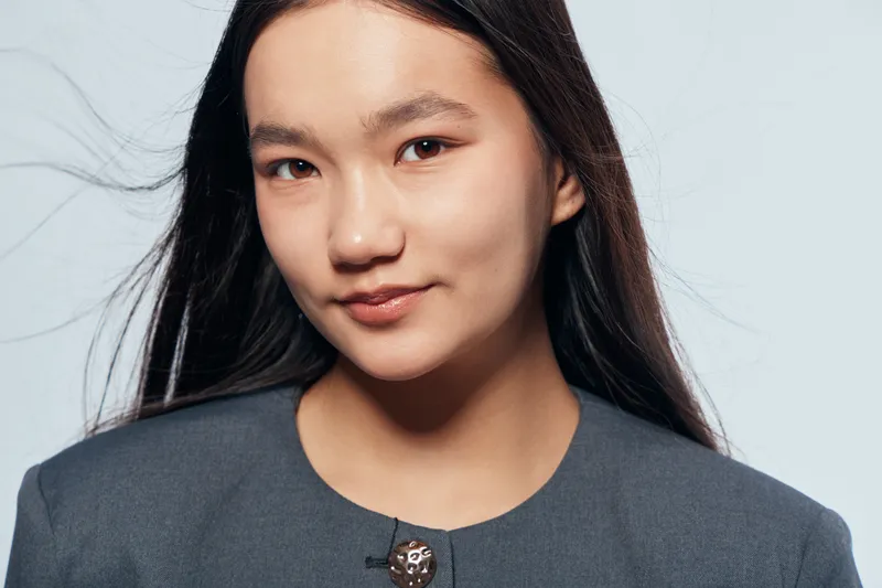Portrait of confident woman with long black hair wearing gray blazer looking at camera with slight smile studio background female face youth beauty elegance and style concept