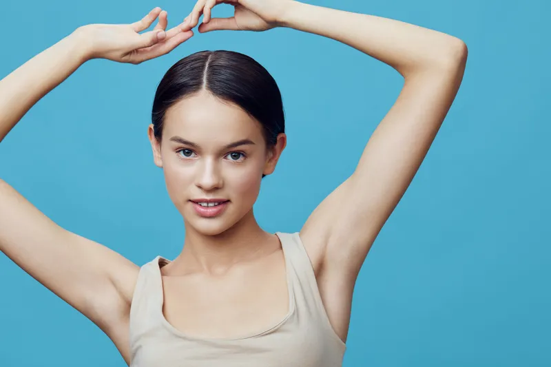 Young female model with long hair posing against a vibrant blue background, showcasing natural beauty and confidence through her smile and graceful gesture, perfect for beauty and skincare themes