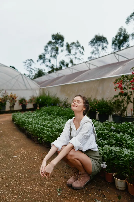 Young woman enjoying nature in a greenhouse, wearing casual clothing, surrounded by plants and greenery, capturing a serene and joyful emotion