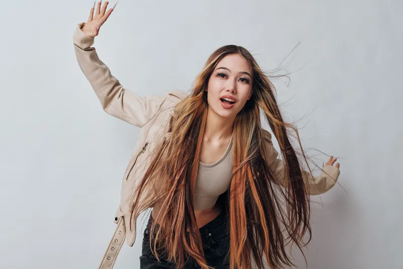 Young woman with long hair and casual jacket posing in motion with expressive face on neutral background for lifestyle and fashion portrait photography.