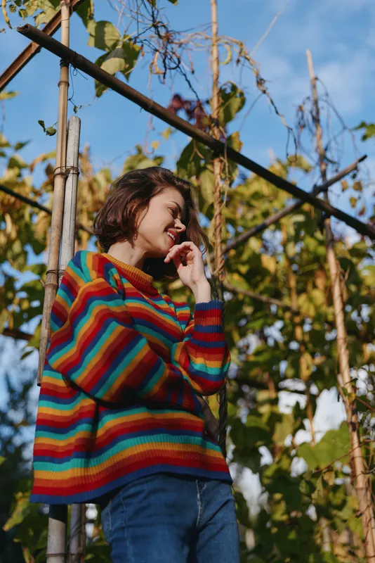 woman striped sweater smile garden autumn casual portrait by vine trellis, young female laughing outdoors in colorful knit pullover, relaxed seasonal fashion