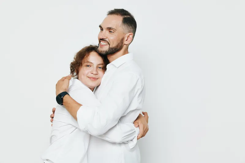A professional man in a white shirt shares a warm embrace with a colleague, showcasing leadership, confidence, and teamwork against an isolated white background.