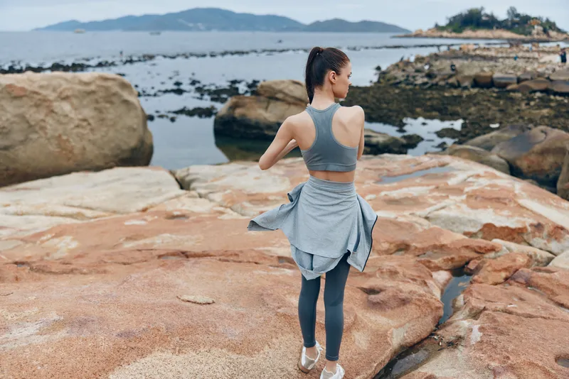 Young woman in athletic wear stretching by the seaside, showcasing a healthy lifestyle and fitness in a serene coastal setting
