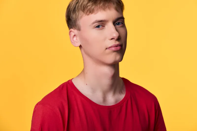 Young man in a red shirt posed against a bright yellow background for fashion and lifestyle photography, studio lighting, clean composition, vibrant color contrast.