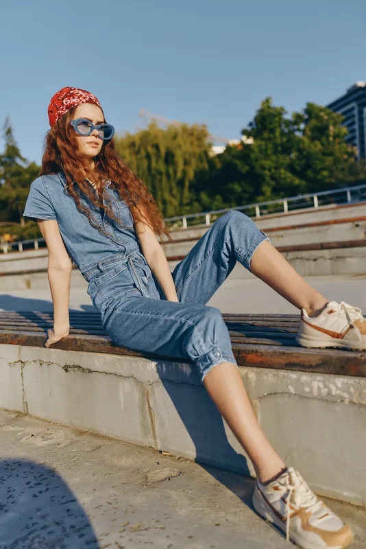 lifestyle woman in modern boho-western denim street style wearing sunglasses and a red headscarf, relaxing outdoors with sunny film color tones