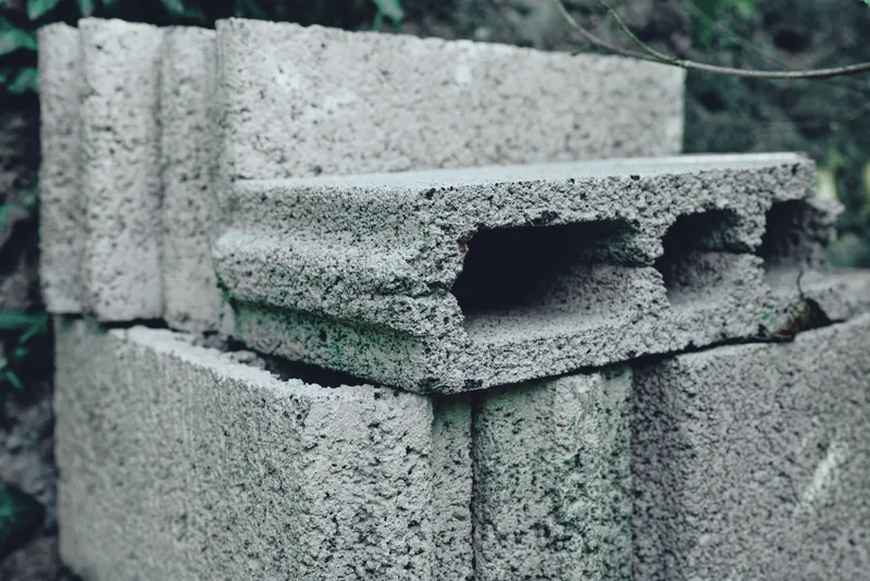 Concrete blocks stacked in a weathered masonry pile, rough texture and hollow cores, outdoor construction material for building walls and foundations