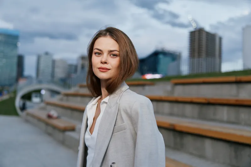 confident young woman in beige business suit outdoors urban background with skyscrapers and cloudy sky in spring season fashion business style