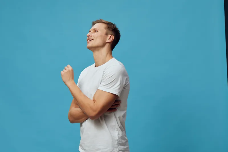 Smiling young caucasian man wear white t-shirt looking up standing crossed arms isolated on blue background digital detox mental health concept expression portrait