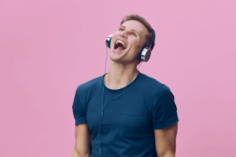 Smiling man wearing headphones enjoying music on pink background, casual clothing, cheerful expression, energetic mood, lifestyle concept, vibrant colors, young adult male.