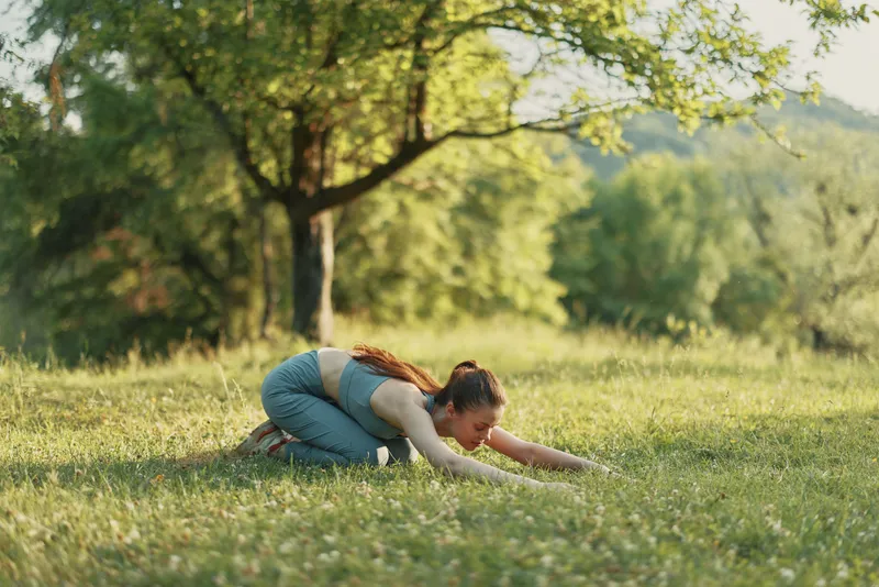 Woman practicing yoga in nature, wearing sportswear, expressing calmness among greenery under sunlight, highlighting wellness and fitness concepts