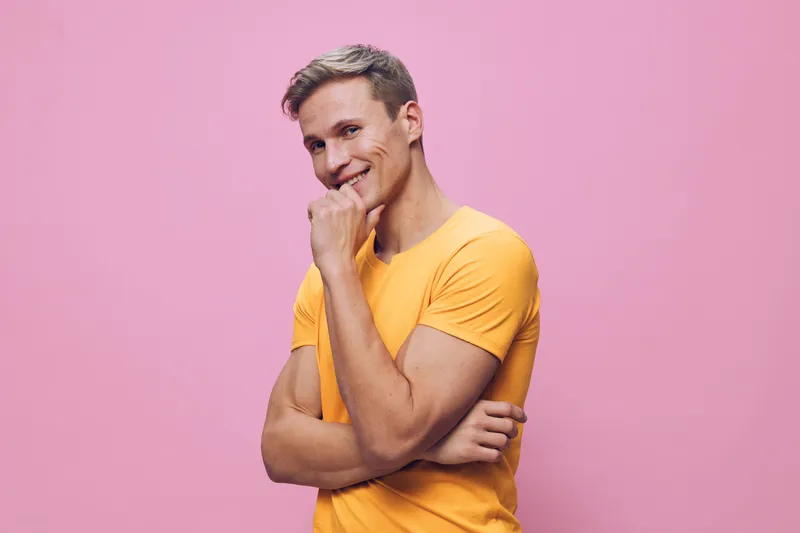 Smiling young caucasian man wearing yellow t-shirt pose pink background casual cheerful friendly digital nomad concept
