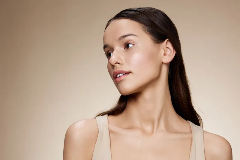 Natural beauty portrait of a young woman with long hair on a neutral background, showcasing healthy skin and a serene expression, ideal for beauty and skincare concepts