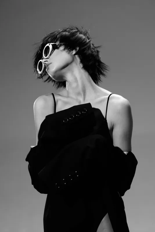 Stylish woman wearing sunglasses and black outfit posing with confident attitude in black and white