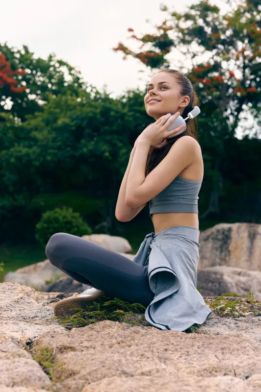 Young woman enjoying healthy lifestyle sitting on rocks, wearing sportswear and smiling, amidst nature, promoting fitness and wellness concepts