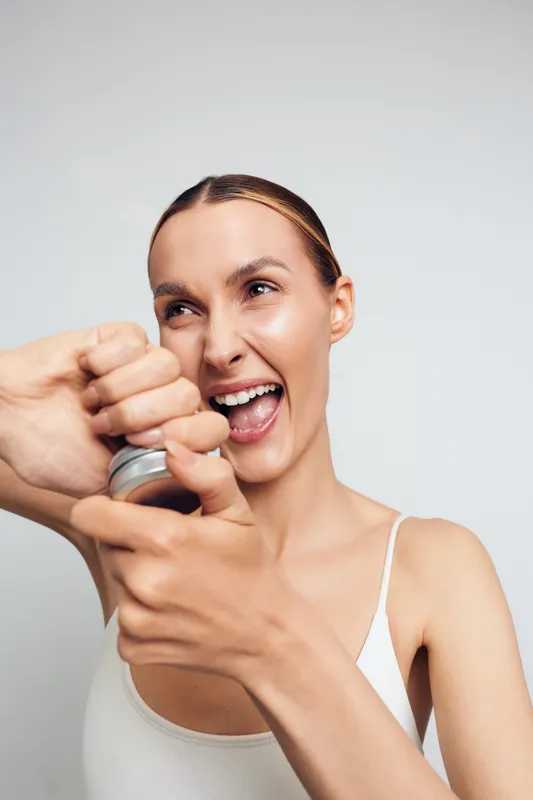 Happy woman opening can with manual opener, smiling with excitement, closeup portrait, bright studio background, casual outfit, natural skin texture, joyful moment