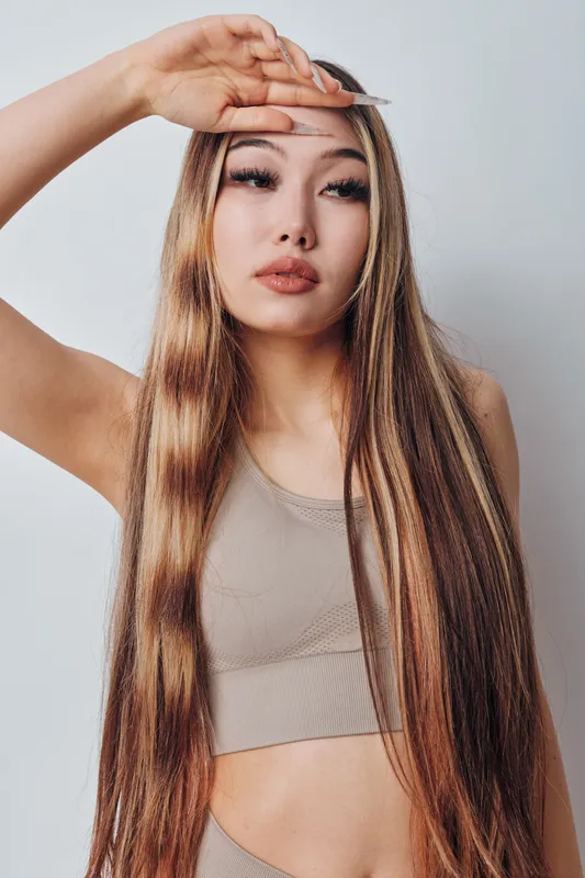 Young woman with long straight hair wearing casual top posing with hand on forehead against light background. Beauty, fashion and portrait with natural look and confident expression.