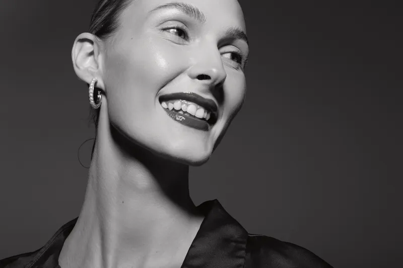 Smiling Caucasian woman with pale skin wearing hoop earrings looks to side in black and white close-up portrait. Concept of happiness, beauty, and elegance.