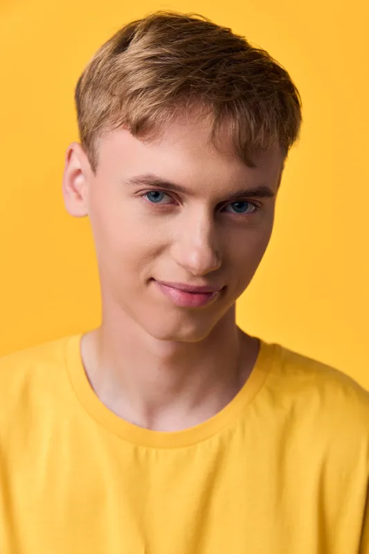 Close-up of a male with a light smile, wearing a yellow t-shirt, against a vibrant yellow studio background, conveying casual style, confidence and fresh energy in a clean studio shot