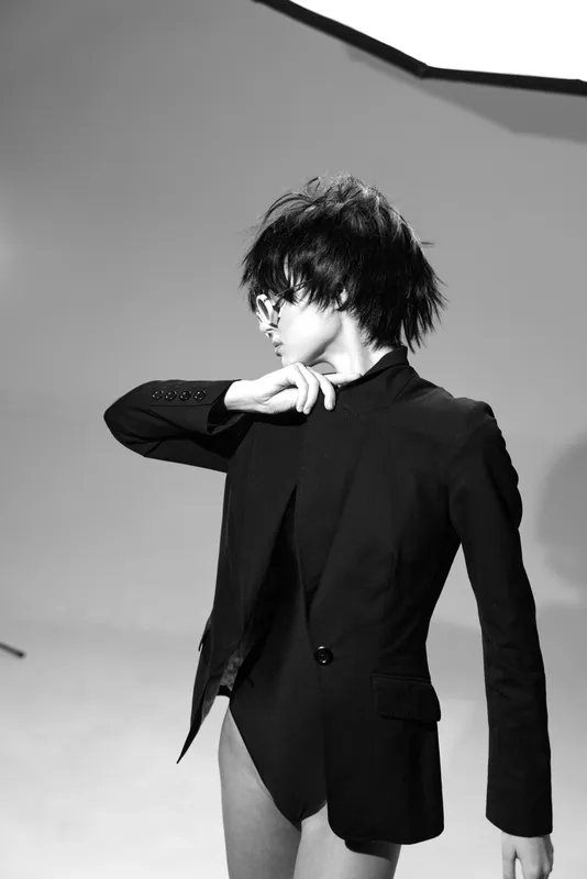 Black and white woman in stylish black jacket posing with short hair in a minimalist studio setting with soft lighting.