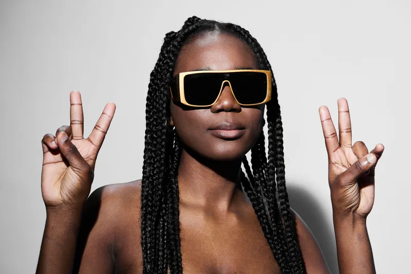 Confident Black Woman in Bold Sunglasses Making Peace Sign Against Minimalist Background