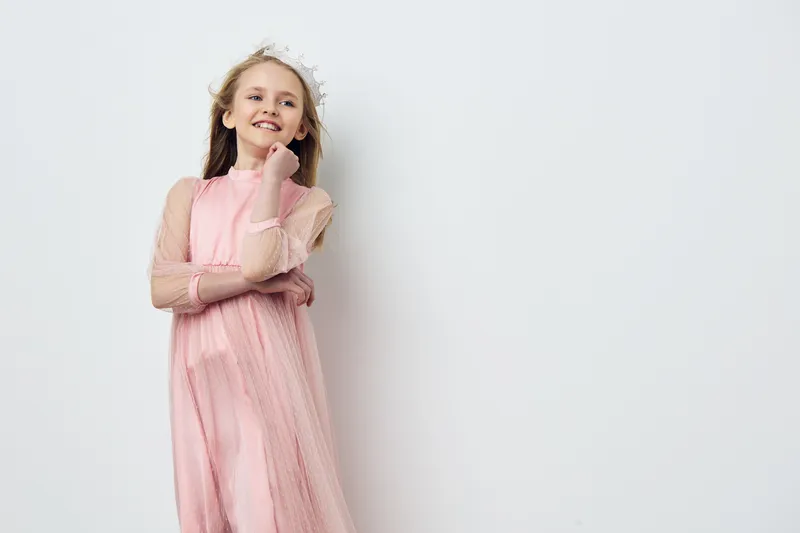 Happy young girl in a pink dress smiling against a light background, embodying innocence and beauty in a playful, joyful moment