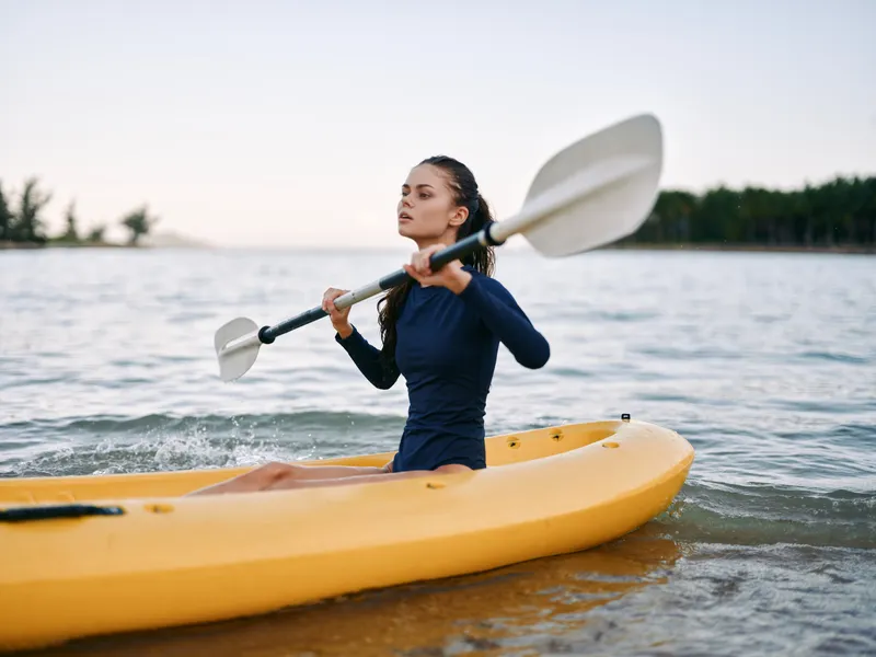 Woman kayaking on the water holding paddle with calm expression, outdoor adventure, nature, active lifestyle, water sport, summer activity