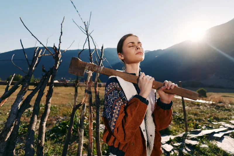 Woman farming in rural field holding a wooden tool on her shoulder, eyes closed and serene, sunlight and mountains in nature background, rustic fence and open landscape.