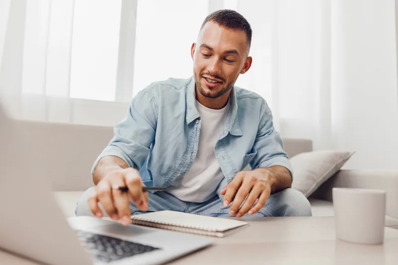 Smiling man engaged in remote work, exhibiting focus and creativity, with a light and airy background that suggests productivity and comfort.