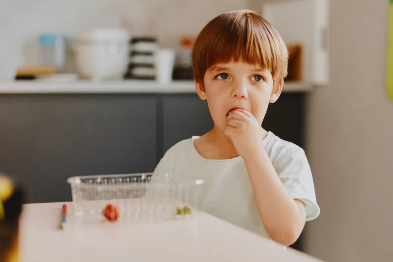 Thoughtful boy enjoying a snack at home in a bright kitchen. The warm lighting enhances the cozy atmosphere and captures a moment of childhood innocence.
