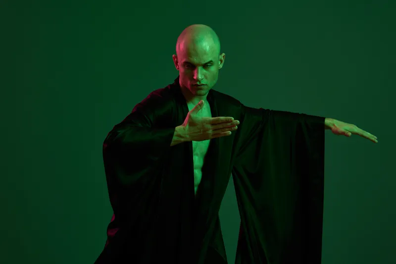Captivating man in black attire performing graceful movements, highlighted by green light in a dark setting. The image reflects elegance and dynamic energy.
