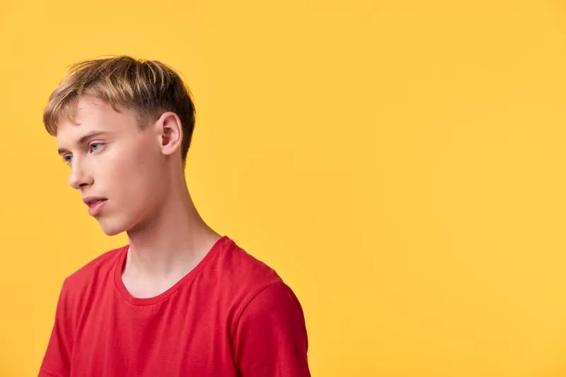 Young man in a red shirt stands against a vibrant yellow backdrop, conveying casual fashion and calm confidence in a studio setting ideal for fashion, lifestyle, and stock photography.