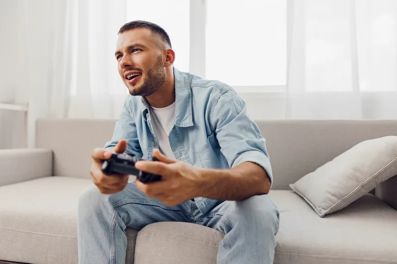Joyful man enjoying a video game while relaxing at home, reflecting a moment of serenity and digital detox from everyday stress and work-life blur.