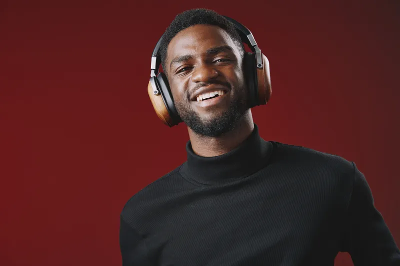 Smiling African American man wearing stylish headphones against a vibrant red background, representing modern technology and joyful music experiences
