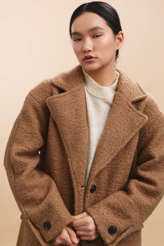 asian woman wearing a warm oversized coat stands in a neutral studio, presenting a calm, confident mood with a minimalist fashion vibe suitable for lifestyle or editorial use.