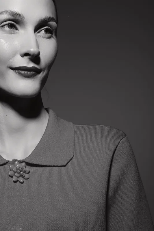 Close-up of a caucasian woman with fair skin wearing a vintage collared sweater and brooch smiling slightly in studio lighting. Concept for retro fashion and elegance.