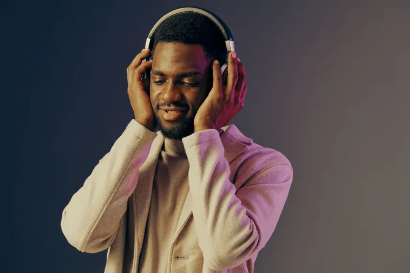 Young African man enjoying music with headphones, expressing joy and relaxation in a vibrant, colorful background, ideal for lifestyle advertisements