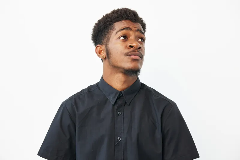 A thoughtful African American man gazes upwards, showcasing a moment of contemplation and inspiration. His stylish black shirt complements his expressive demeanor beautifully.