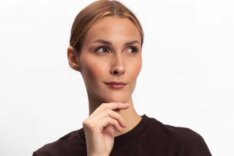 Thoughtful young woman with blonde hair and clear skin looks away with hand on chin. Portrait on white background. Concept of contemplation, decision making, and beauty.