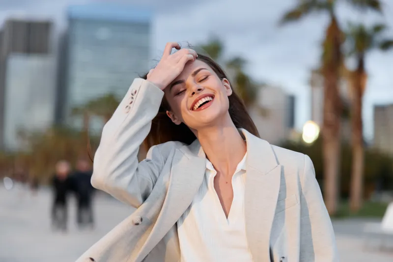 cheerful woman in business casual outfit enjoying urban outdoor setting with joyful smile and relaxed pose in modern city environment