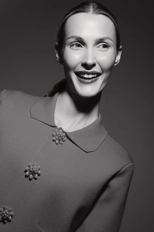 Smiling caucasian woman with light skin and slicked hair wears vintage dress with floral buttons in black and white portrait.