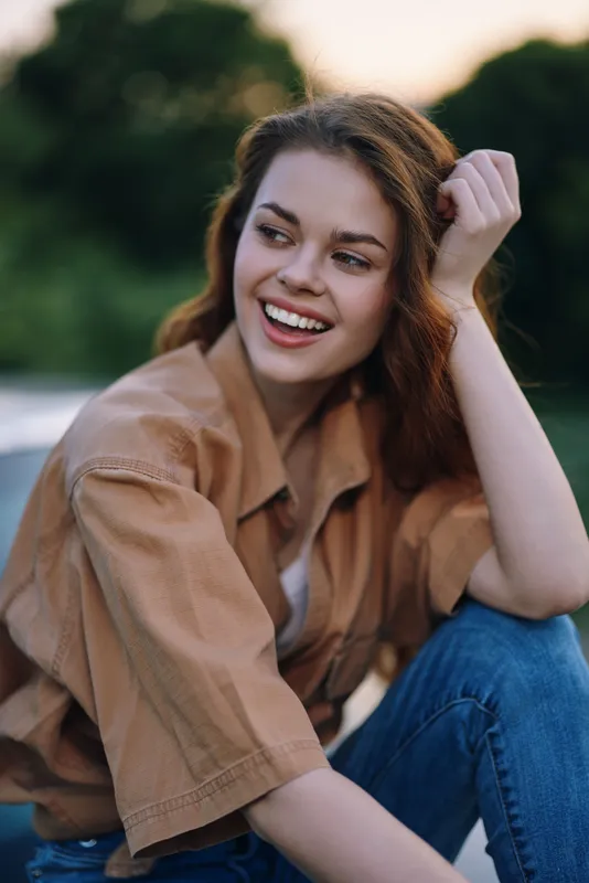 Smiling young woman in casual outfit, enjoying summer outdoors with a relaxed pose and vibrant green background, embodying happiness and tranquility.