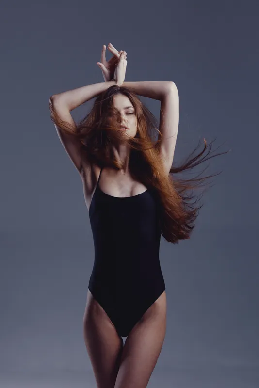 graceful woman in black swimsuit posing with closed eyes and flowing hair, serene expression, studio background