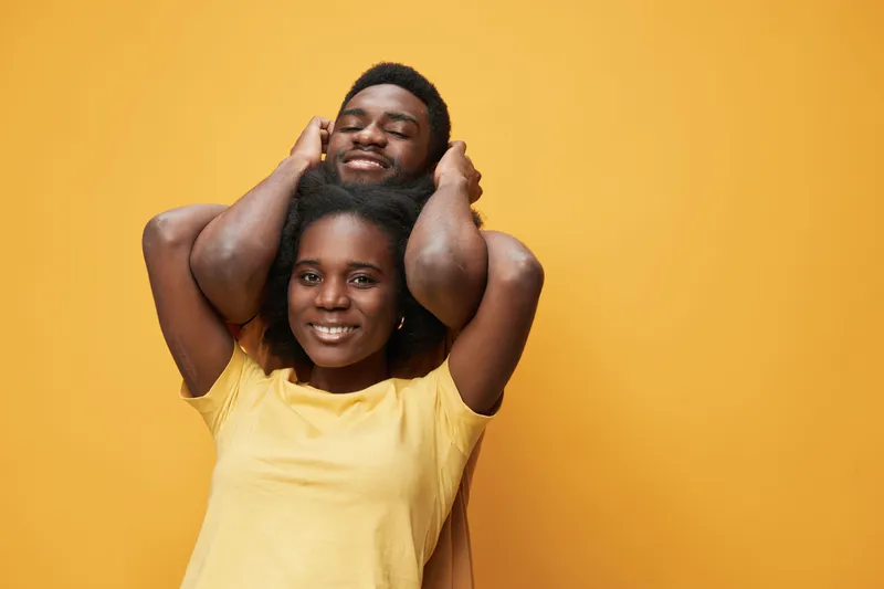 Happy couple with cheerful expressions in matching yellow outfits against a vibrant yellow background, showcasing love and connection