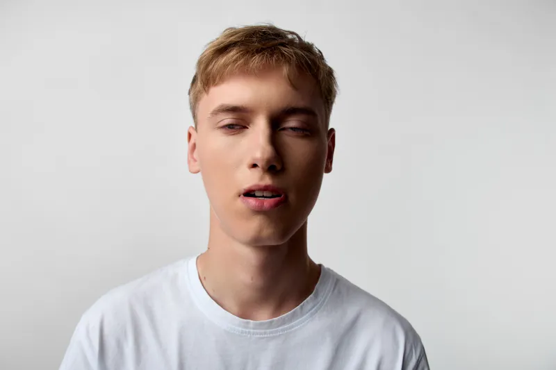 Young male face closeup with neutral expression, casual tshirt, soft studio background, subtle lighting and relaxed mood, simple composition for profile or portfolio use