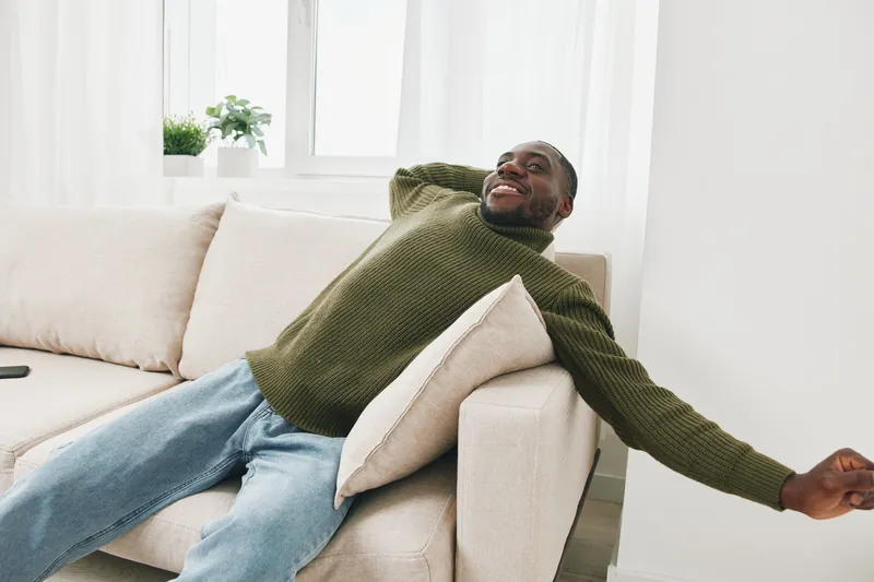 Relaxed man in a cozy sweater expressing happiness in a bright living room, embodying comfort, joy, and serenity during winter season