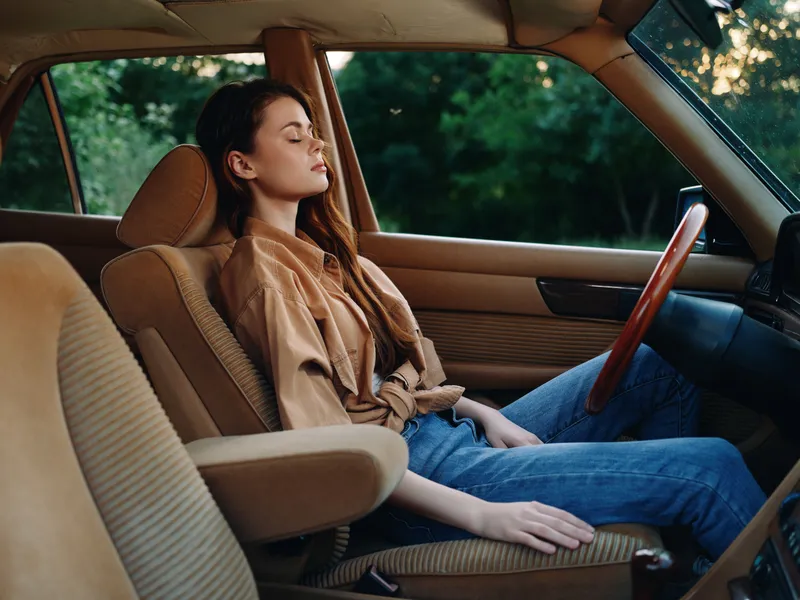 Relaxed young woman in casual clothing sitting in a vintage car, enjoying moments of solitude in nature with calm expressions and earthy color tones.